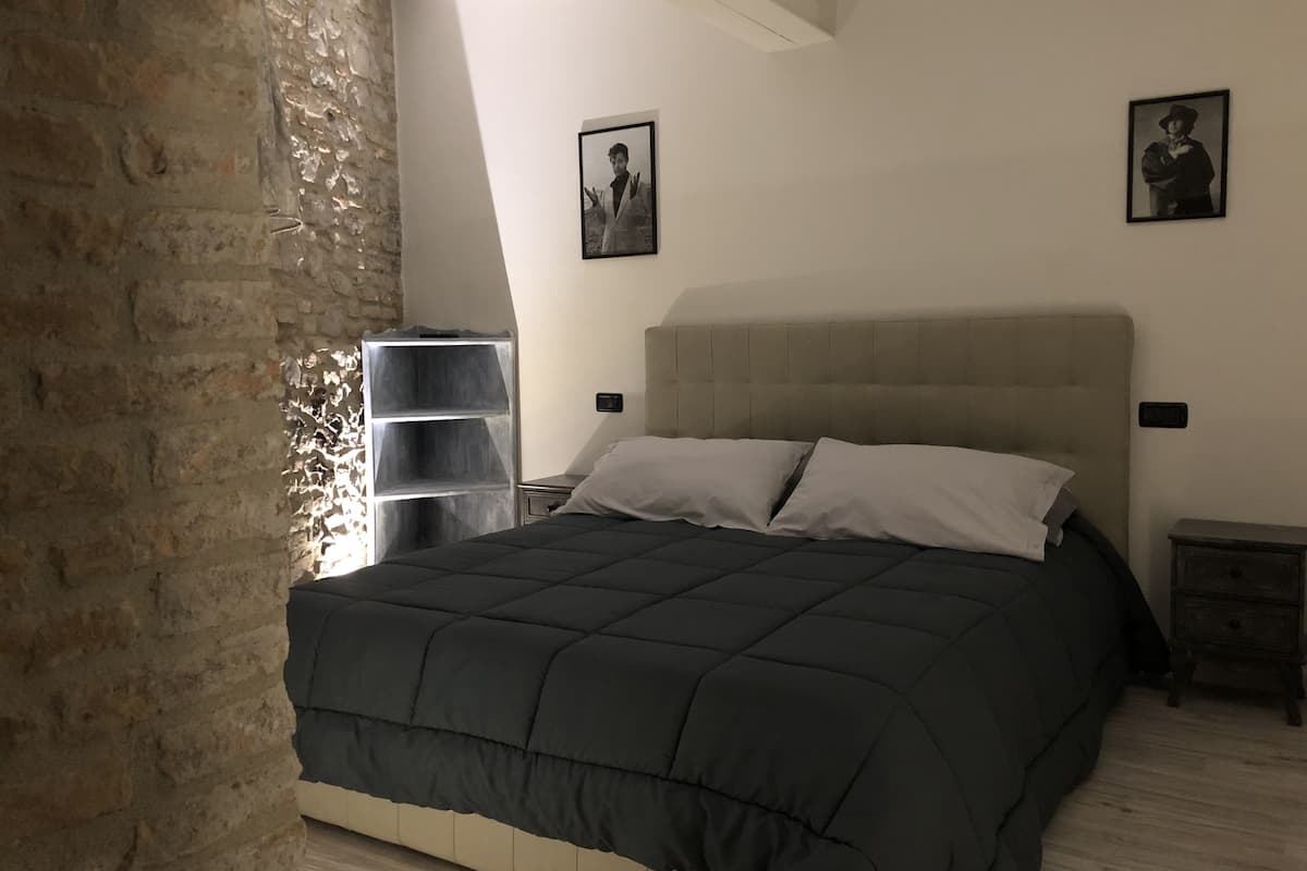Quarto com uma cama grande, mesa de cabeceira, cômoda e duas fotos emolduradas na parede.