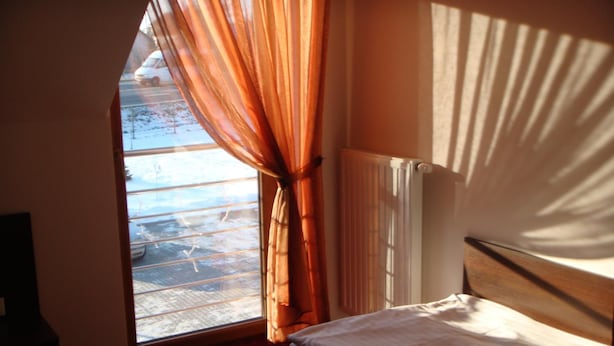 A room with a bed, a window with curtains, a radiator, and a view of a snowy landscape. - Gosciniec Europejski (Miedziana Góra)