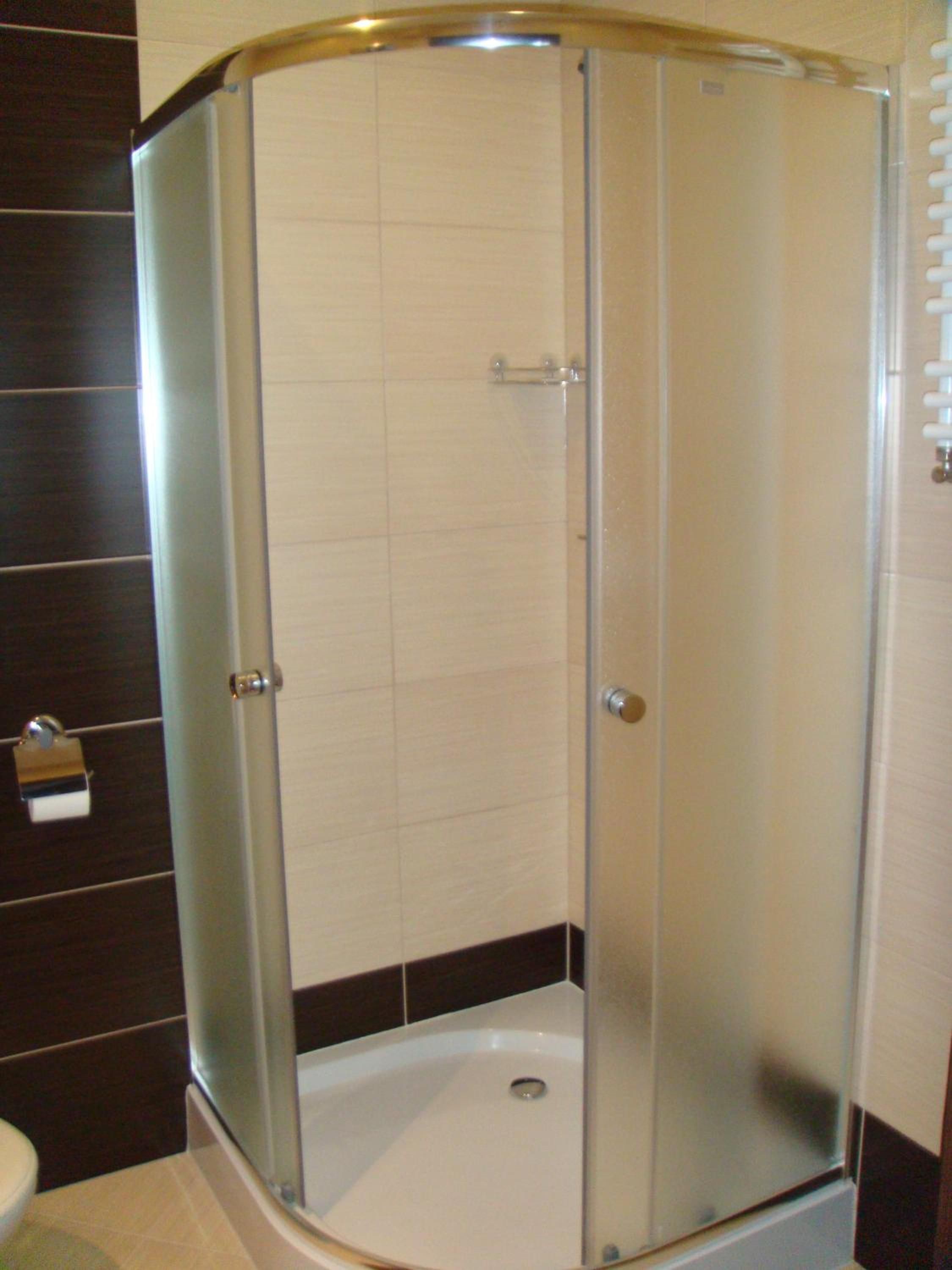 Une cabine de douche fermée par des parois en verre, avec un sol blanc, un porte-serviettes et une porte dotée d’une poignée.