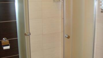 Une cabine de douche fermée par des parois en verre, avec un sol blanc, un porte-serviettes et une porte dotée d’une poignée.
