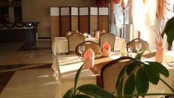 Un área de comedor con mesas dispuestas para dos, sillas y un separador decorativo.