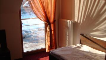 Una habitación con cama, ventana con cortinas, radiador y vista a un paisaje nevado.