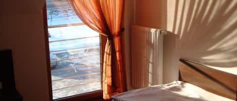 A room with a bed, a window with curtains, a radiator, and a view of a snowy landscape.