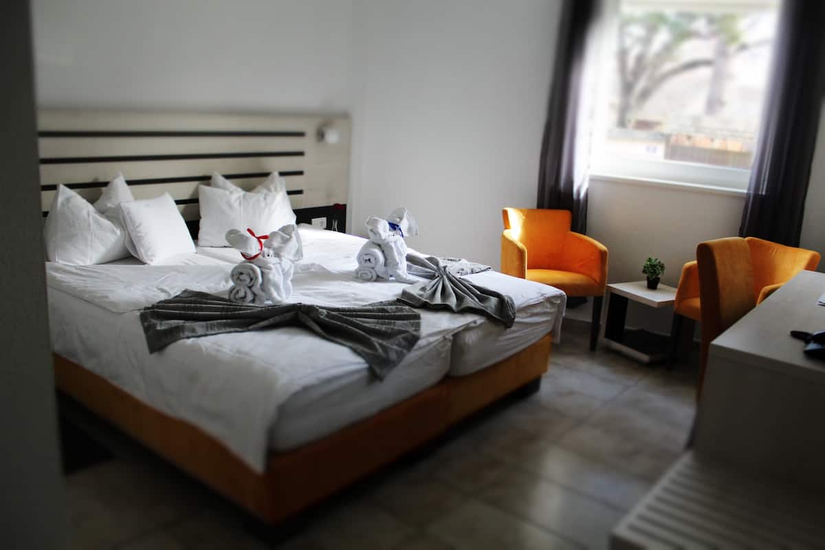 A hotel room with a bed, pillows, a bedside table, a chair, and a window.