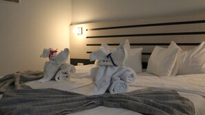 A hotel room with a neatly made bed, a headboard with horizontal lines, and two towels shaped like animals. - Garni Hotel 11Tica DM (Novi Sad)