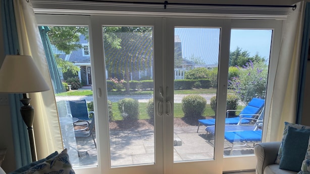 Un salón con sofá, una mesa de centro y vistas a un patio exterior con sillas reclinables azules y un jardín.