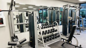 Ein Fitnessstudio mit verschiedenen Trainingsgeräten, darunter Kurzhanteln, Bänke und Kraftgeräte.