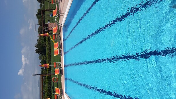 A swimming pool with clear blue water, surrounded by a grassy area with orange umbrellas and a lifebuoy. - Large four-room apartment with swimming pool near the sea (Vada)