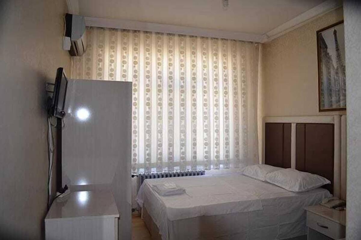 A hotel room with a bed, a radiator, a television, and a window with curtains.