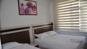 Habitación de hotel con dos camas, una mesita de noche, una obra de arte floral enmarcada y una ventana con persianas.