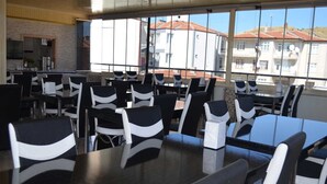 Un comedor con mesas y sillas, ventanas amplias y vistas a edificios.