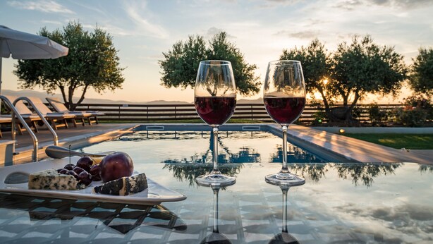 Ein Tisch mit zwei Weingläsern und einer Käseplatte am Pool mit Blick auf den Sonnenuntergang.