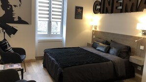 Un dormitorio con cama, una silla, un escritorio, un ventanal con persianas y una pared con un cartel de 'CINEMA'.