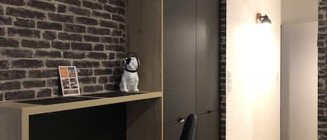 A modern room with a brick wall, a wooden desk with two black chairs, a wardrobe, and a door with a sign.