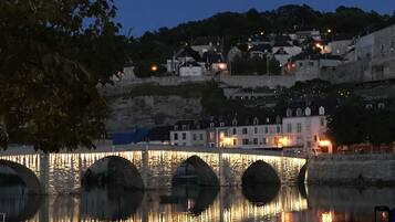A stone bridge over water with buildings on a hillside in the background.