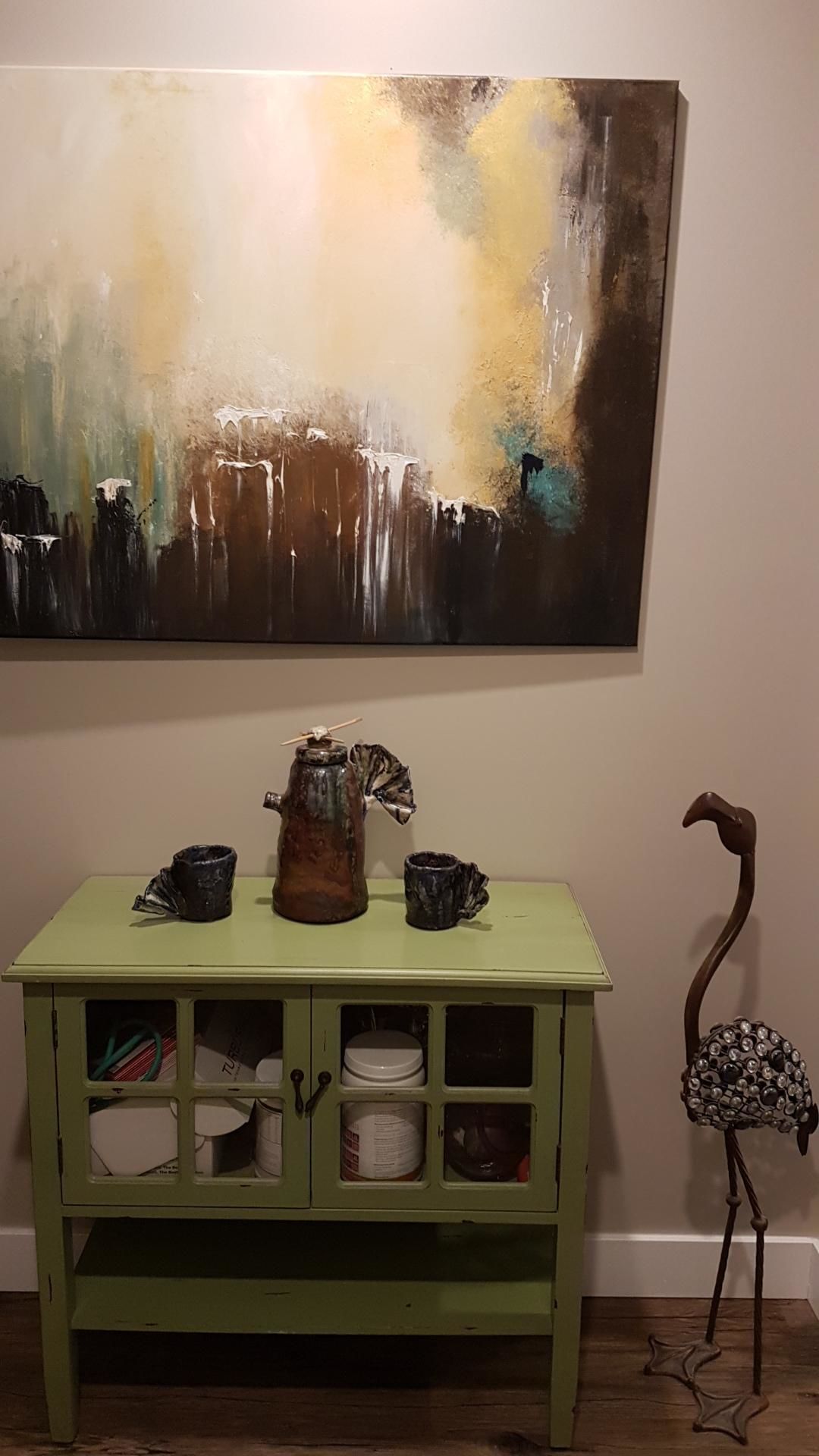 Un gabinete verde con puertas abiertas, una escultura decorativa y un cuadro en la pared.