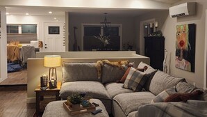 Ein gemütliches Wohnzimmer mit einer Eckcouch, einem kleinen Tisch mit Lampe und einer Zierpflanze.