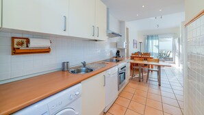 A modern kitchen with white cabinets, a wooden countertop, a dishwasher, an oven, and a dining area with a table and chairs. - Apartment in Hacienda Golf Islantilla Urbanization (Isla Cristina)