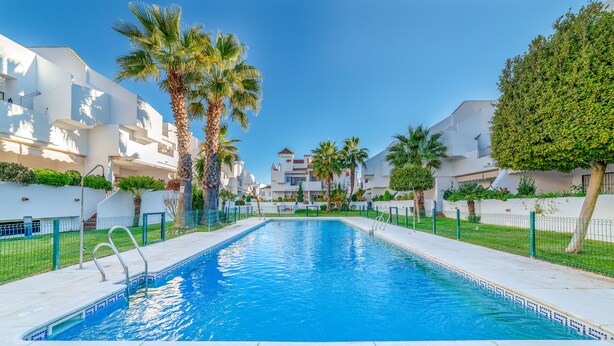 A swimming pool with a clear blue water, surrounded by white buildings and palm trees. - Apartment in Hacienda Golf Islantilla Urbanization (Isla Cristina)