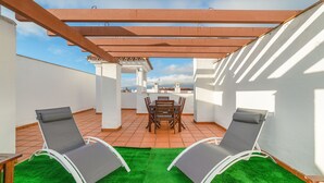 A rooftop terrace with a pergola, a dining table with chairs, and two lounge chairs. - Apartment in Hacienda Golf Islantilla Urbanization (Isla Cristina)