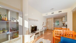 A modern living room with a TV, wooden furniture, and a glass cabinet with kitchen items. - Apartment in Hacienda Golf Islantilla Urbanization (Isla Cristina)