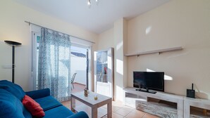 A living room with a blue sofa, a white coffee table, a flat-screen TV, and a sliding glass door leading to a balcony. - Apartment in Hacienda Golf Islantilla Urbanization (Isla Cristina)