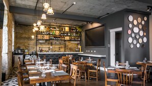 A restaurant with wooden tables and chairs, a bar area with shelves of bottles, and a wall with decorative plates.