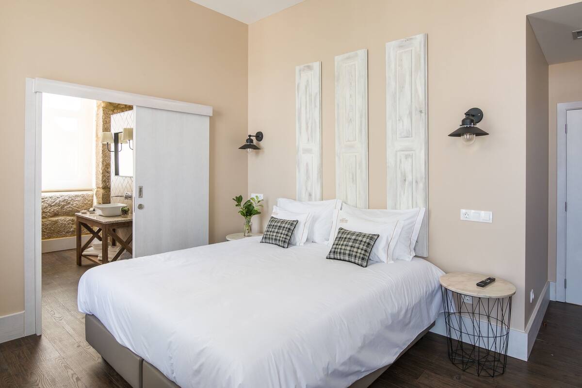 A bedroom with a large bed, a small table with a lamp, and a view of a balcony.