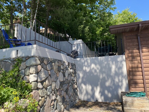 Un mur de soutènement en pierre, agrémenté d’une rambarde métallique, d’une terrasse en bois et d’un petit abri de jardin.