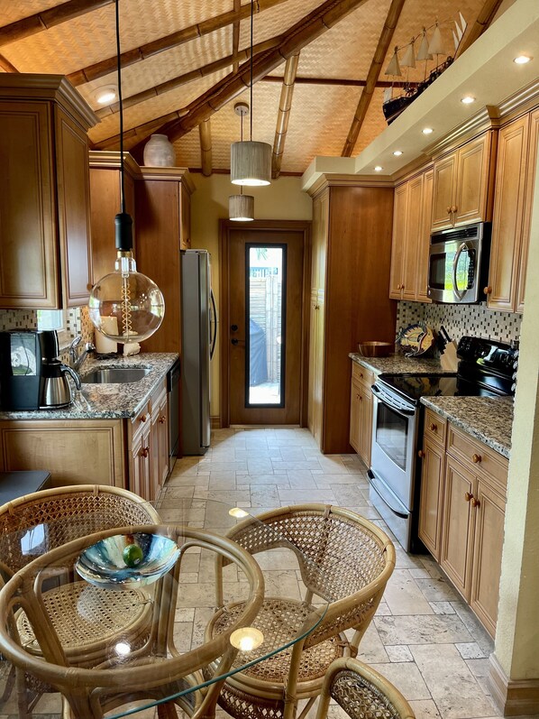 A kitchen with wooden cabinets, a stainless steel refrigerator, a microwave, and a stove. There is a wicker table with chairs and a glass bowl.