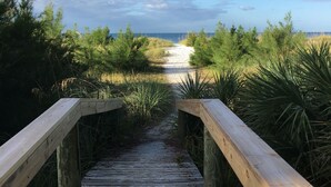 Ein Holzsteg führt zu einem Strand unter blauem Himmel.