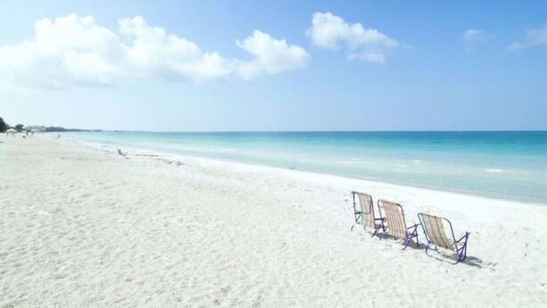 Ein Strand mit weißem Sand und eine Reihe Liegestühle, die zum Meer ausgerichtet sind.