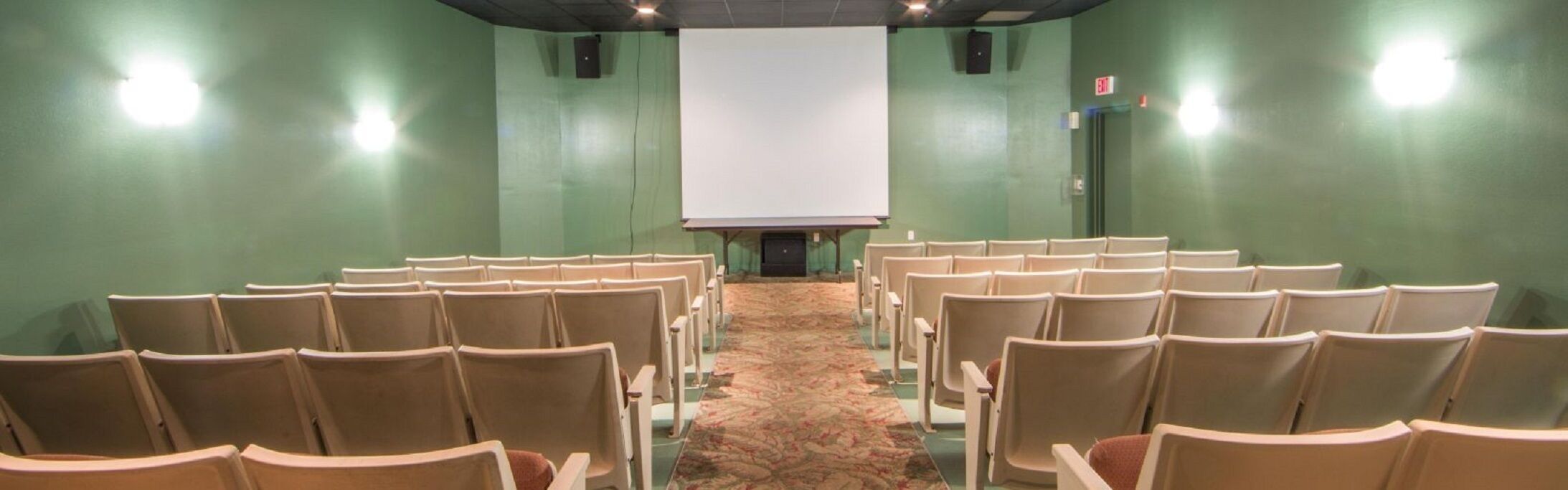 A conference room with rows of chairs facing a large white projection screen.