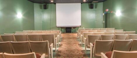 A conference room with rows of chairs facing a large white projection screen.