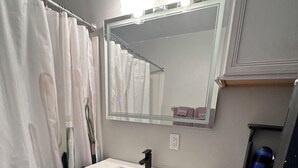 Un baño con un lavamanos blanco, un espejo, un inodoro y una cortina de ducha.