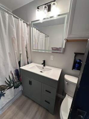Une salle de bain avec un lavabo blanc, un miroir, des toilettes et un rideau de douche.