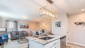 Et moderne køkken med en central ø, et spiseområde med sofa og stole, og en stue med sofa og kunstværker.