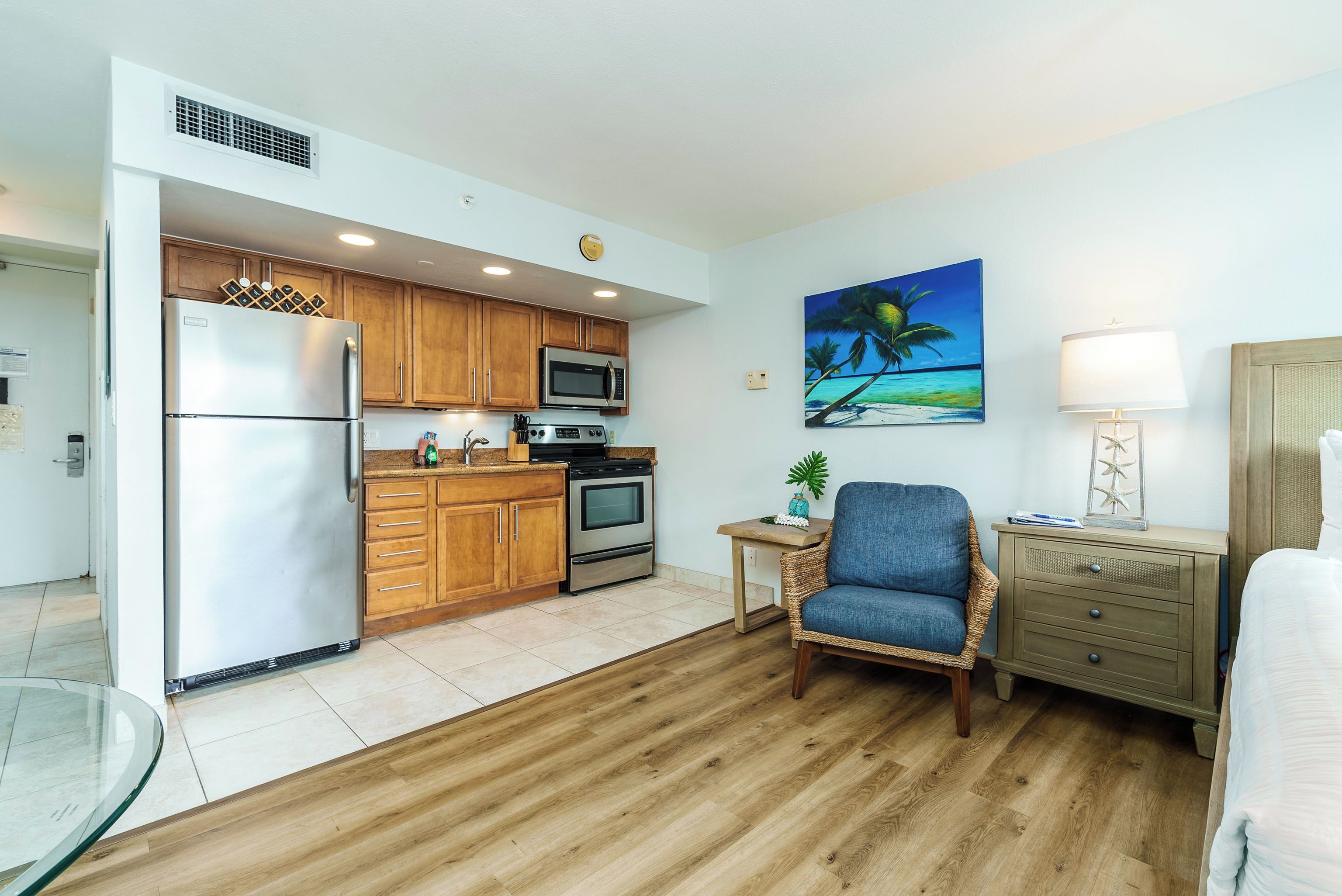 Una cocina compacta con armarios de madera, electrodomésticos de acero inoxidable y un pequeño comedor con una silla de mimbre.