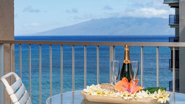 Een tafel met een champagnefles, twee glazen en een bloemstuk op een balkon met uitzicht op zee.