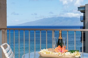 Een tafel met een champagnefles, twee glazen en een bloemstuk op een balkon met uitzicht op zee.