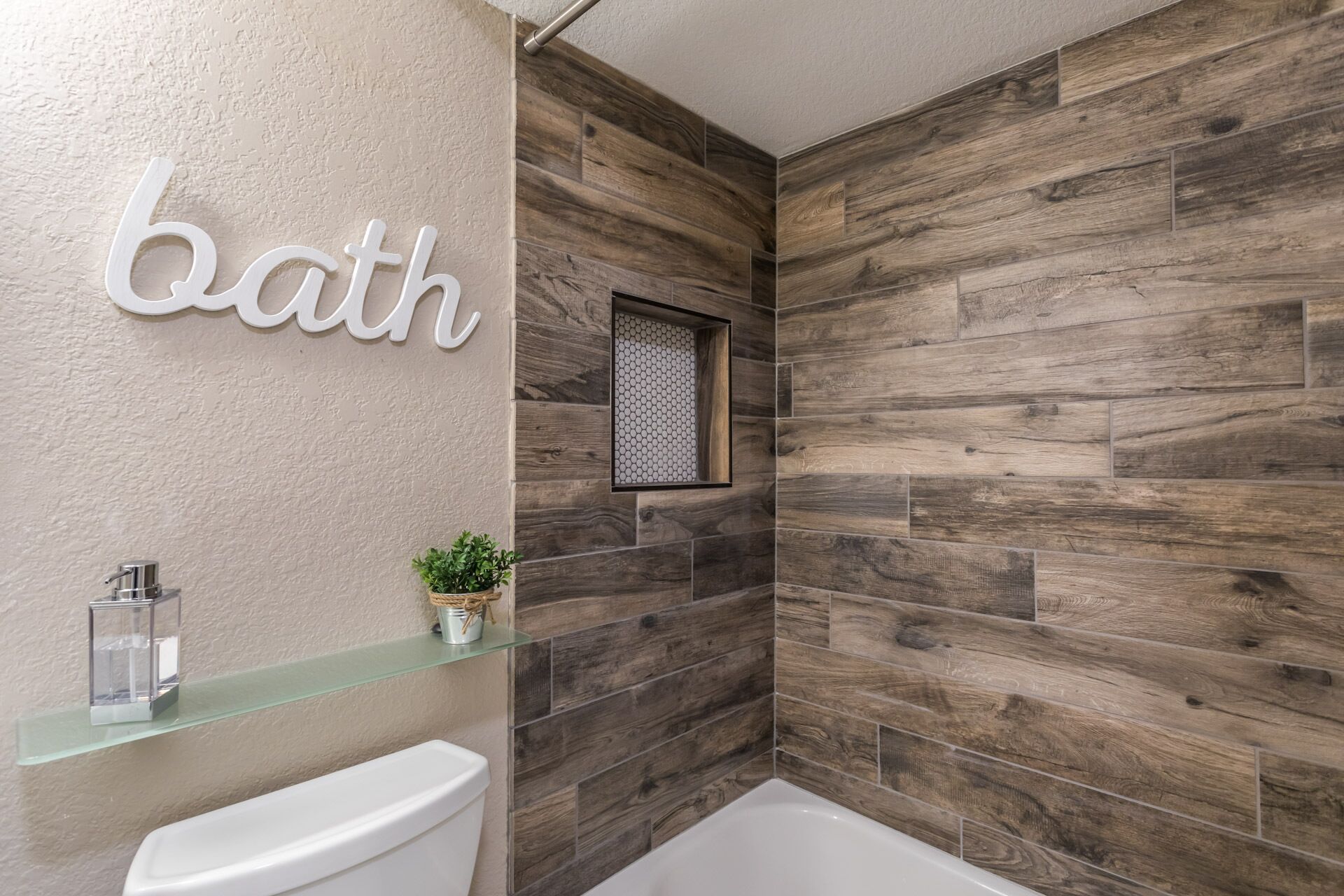 Une salle de bain avec un mur en bois, des toilettes, une étagère en verre avec une plante et un tableau encadré.