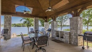 An outdoor patio with a stone fireplace, a grill, and a table with chairs.