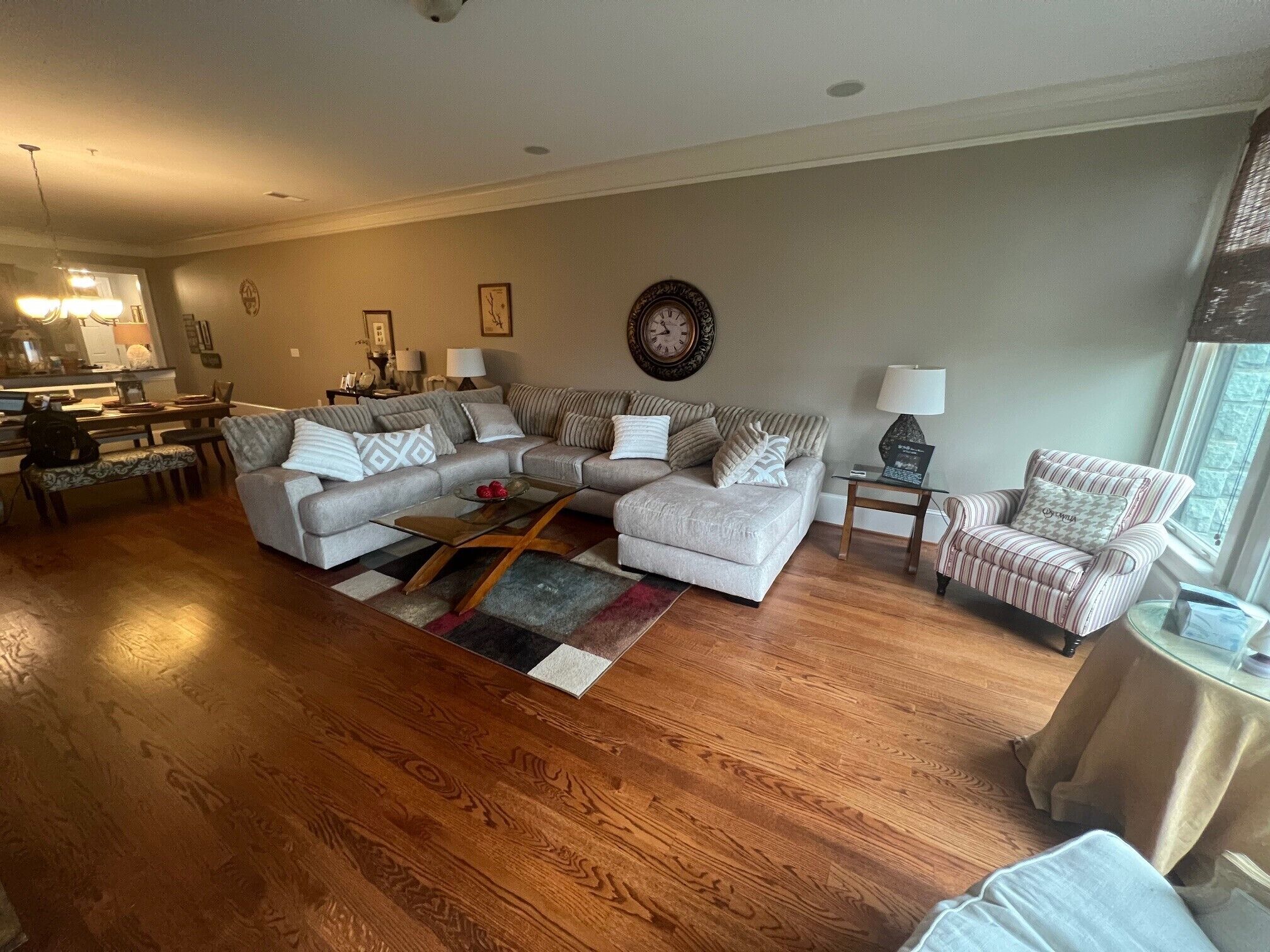 A spacious living room with a large sectional sofa, a coffee table, and a striped armchair. A dining area with a table and chairs is visible in the background.