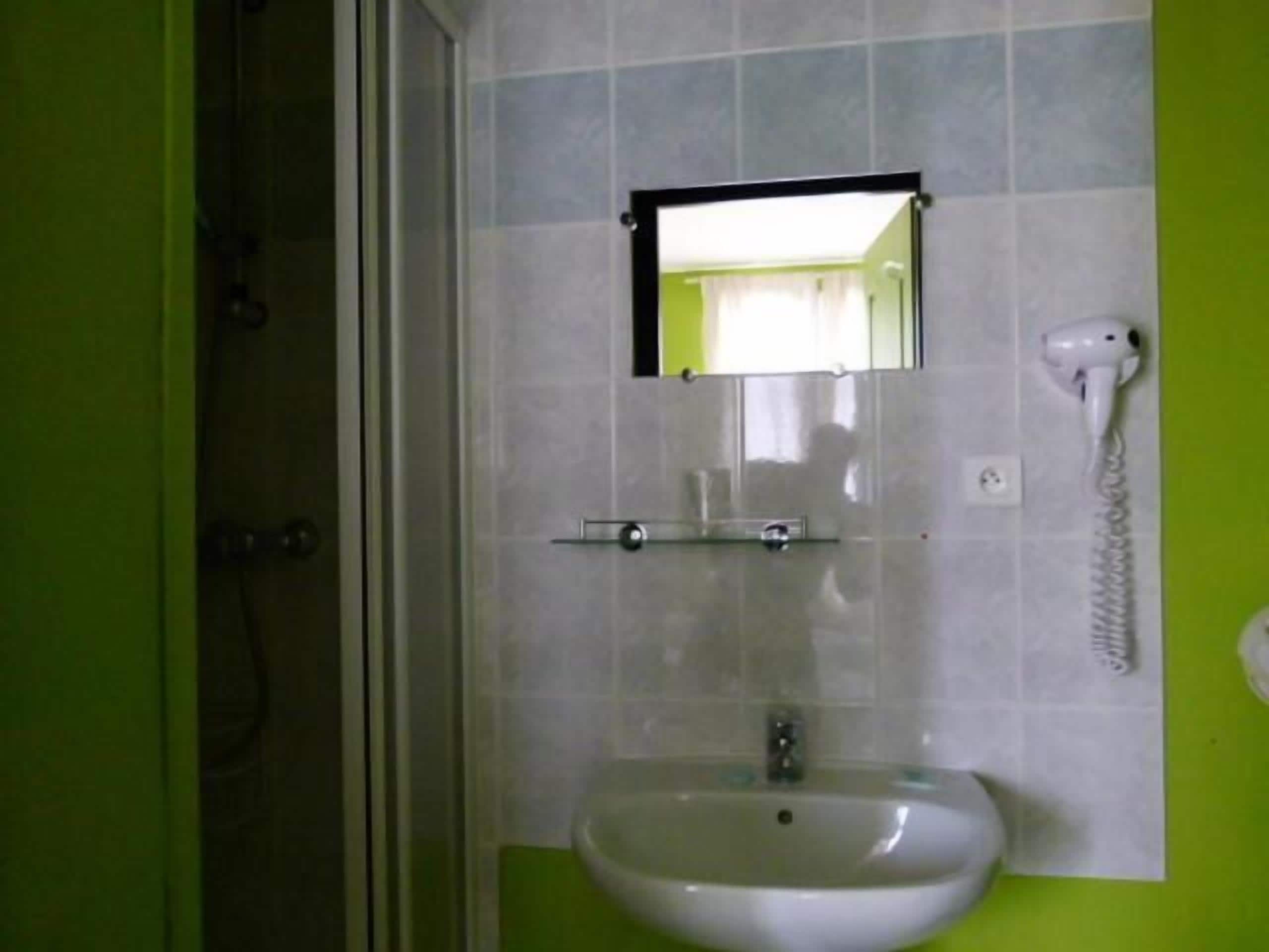 A bathroom with a white sink, a mirror, and a hairdryer on the wall.