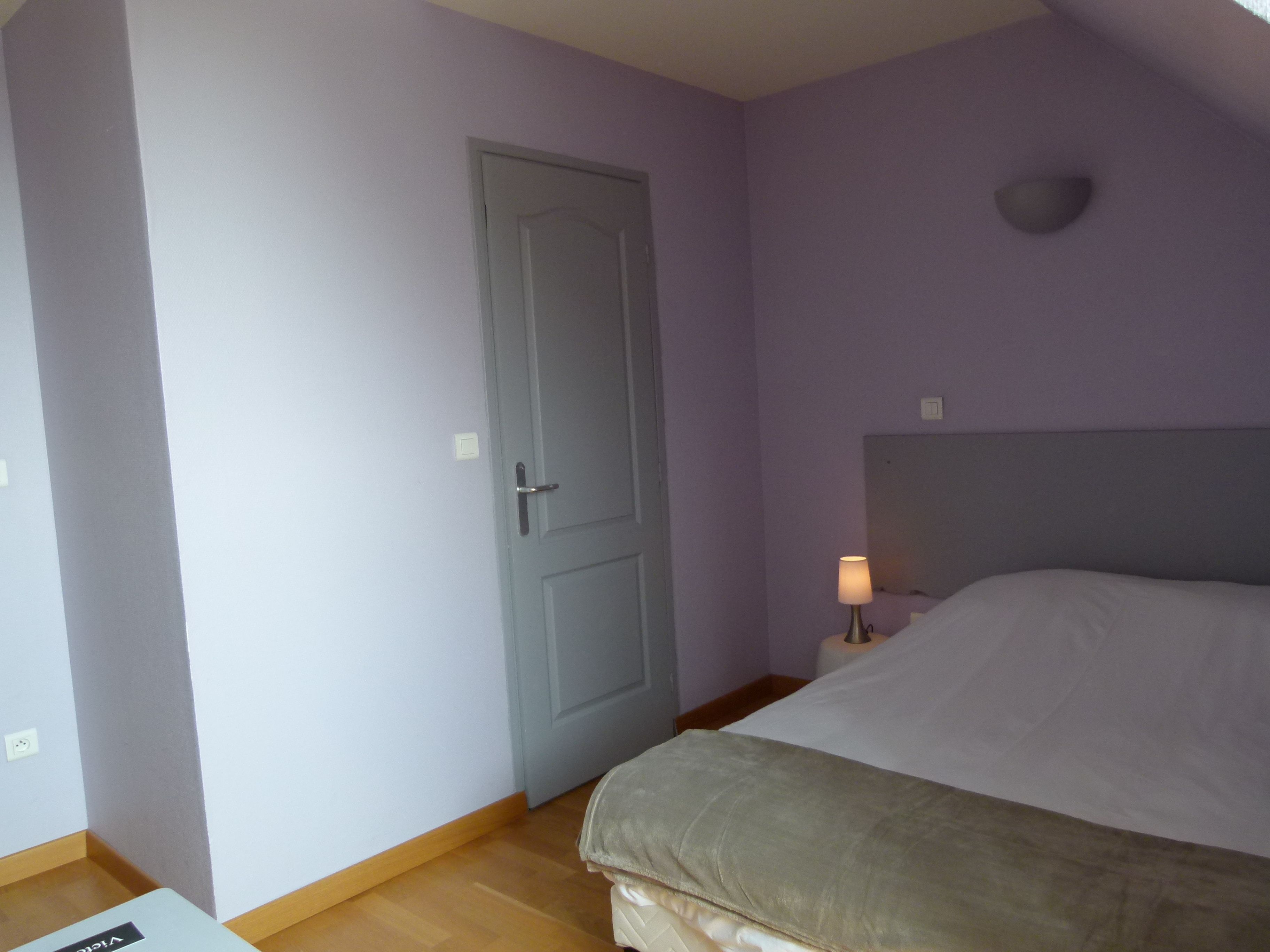 Un dormitorio con una cama, una puerta, una mesita de noche con lámpara y una lámpara de pared.