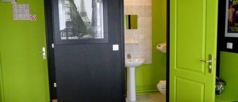 Una habitación con una cama, una puerta verde, una pared negra y un cuadro enmarcado de un paisaje urbano.