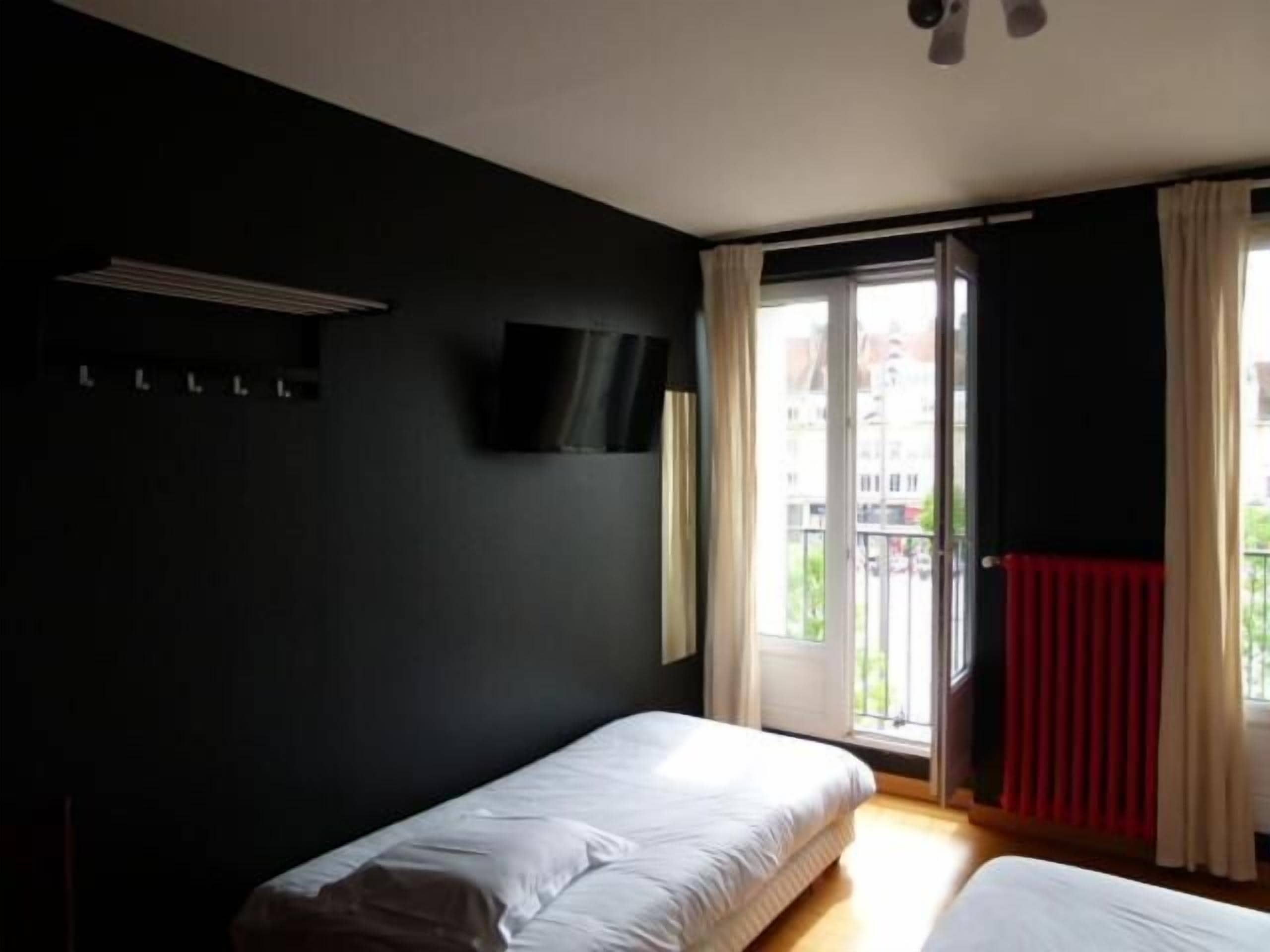 A bedroom with two beds, a TV on the wall, and a window with curtains.