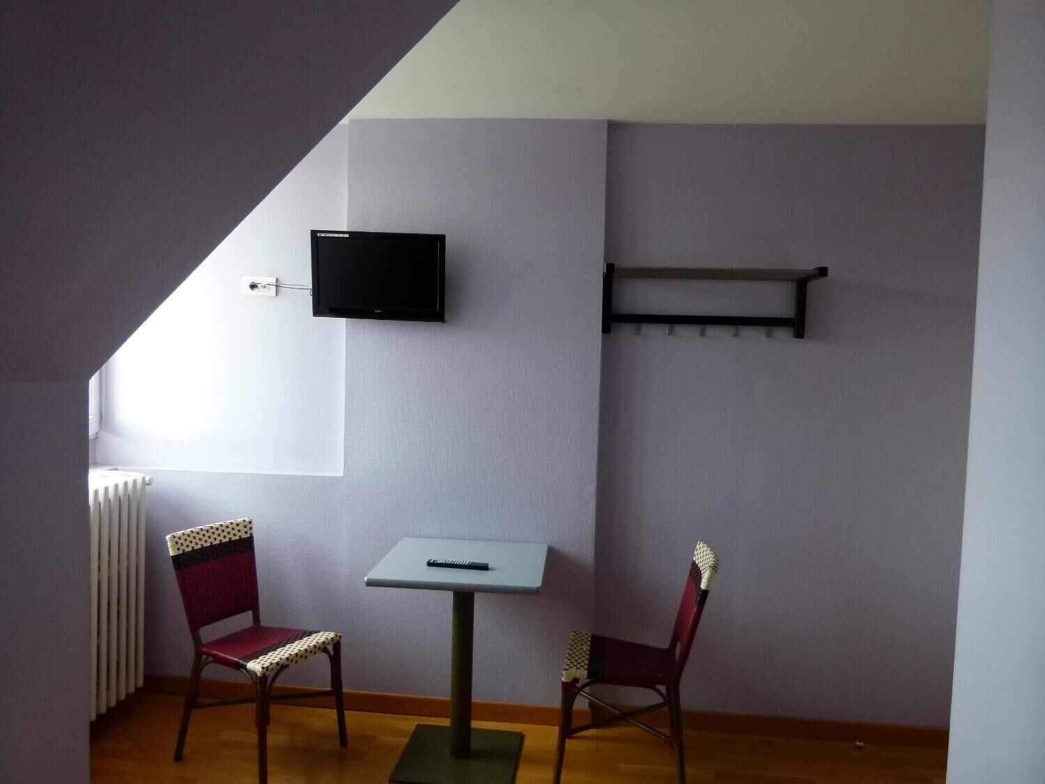 Una habitación pequeña con televisión en la pared, una mesa, dos sillas y un radiador.