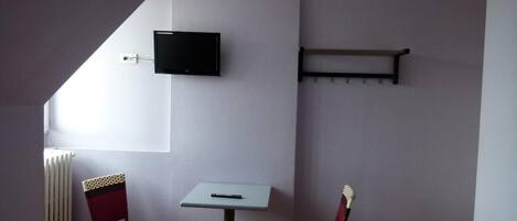 A small room with a TV mounted on the wall, a table, two chairs, and a radiator.