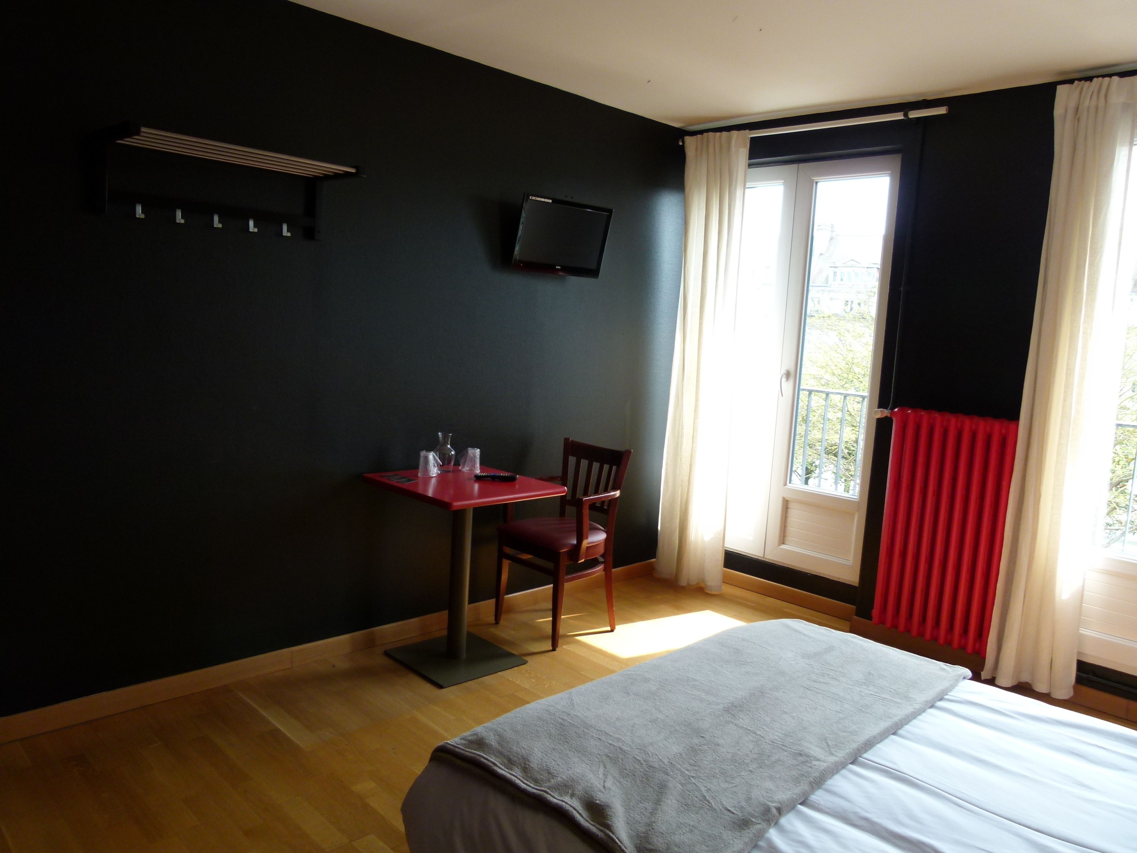 Une chambre d’hôtel avec un lit, un bureau et une chaise, un téléviseur fixé au mur et une fenêtre avec des rideaux.